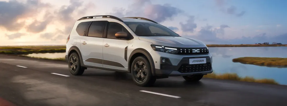 Dacia Jogger gris clair roulant sur une route au bord de l’eau au coucher du soleil