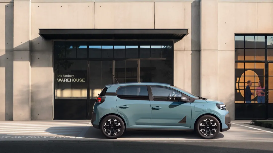Dacia Spring de deuxième génération bleu clair vue de profil, garée devant un bâtiment en béton