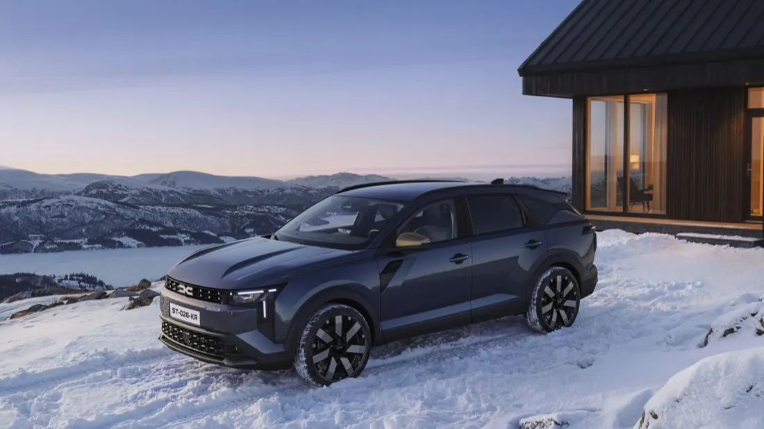 Dacia Striker gris foncé garé sur la neige devant un chalet, vue de trois quarts avant