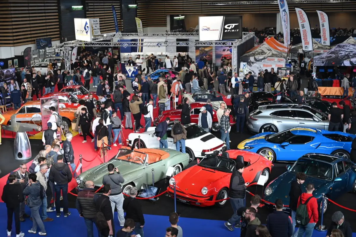 Foule dans une allée d’Epoqu’Auto autour de voitures de sport anciennes exposées sur moquette bleue
