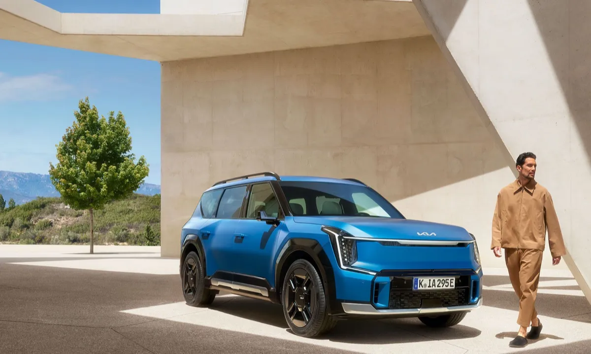 Kia EV9 bleu garé à l’ombre d’une architecture en béton, vue de trois quarts avant
