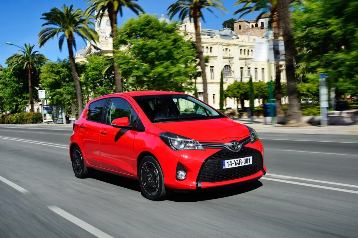 Toyota Yaris de troisième génération dans sa version restylée de 2014, rouge, roulant dans une avenue bordée de palmiers