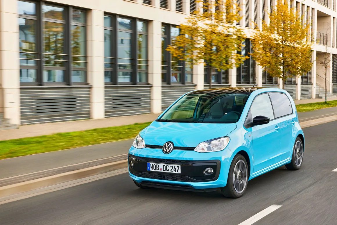Volkswagen up! bleu ciel restylée roulant dans une rue bordée d’immeubles