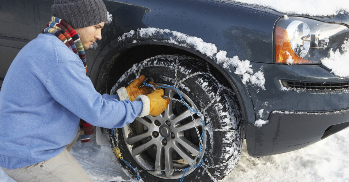 Automobiliste en gants posant une chaîne à neige sur la roue avant d’une voiture enneigée
